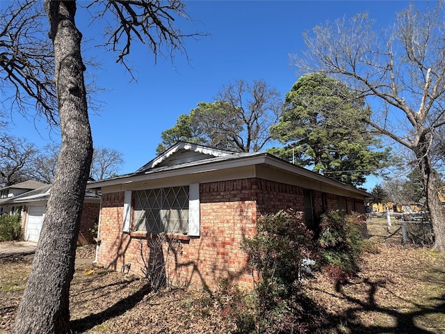 view of side of home with brick siding, a garage, and fence