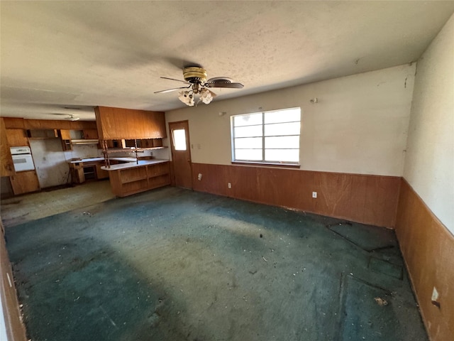 kitchen featuring brown cabinetry, a wainscoted wall, ceiling fan, wood walls, and a textured ceiling