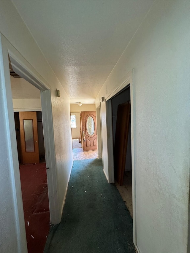 hall featuring a textured ceiling and a textured wall