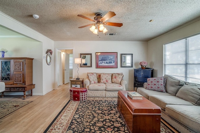 living area featuring visible vents, crown molding, ceiling fan, light wood-style floors, and a textured ceiling