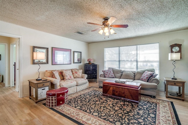 living area with visible vents, ornamental molding, a ceiling fan, a textured ceiling, and light wood finished floors