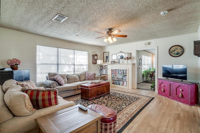 living room featuring visible vents, a textured ceiling, wood finished floors, and ornamental molding