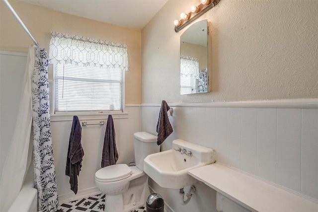 full bath featuring toilet, a healthy amount of sunlight, shower / tub combo with curtain, and wainscoting