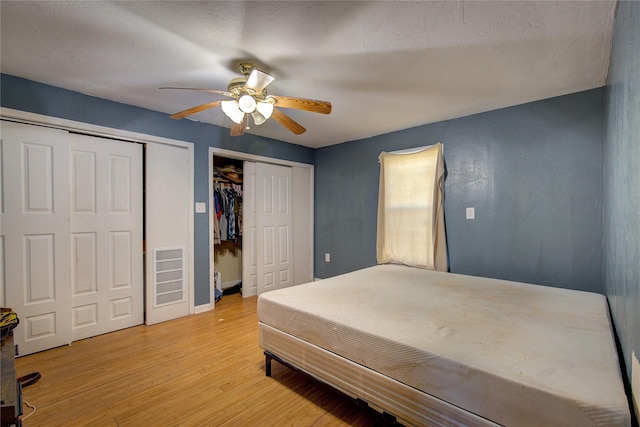 bedroom with baseboards, visible vents, light wood-style flooring, ceiling fan, and multiple closets