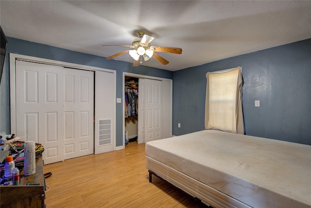 bedroom with light wood finished floors, visible vents, two closets, and ceiling fan