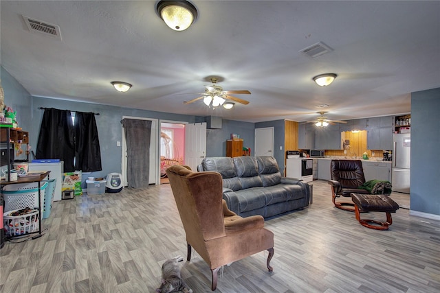 living room with visible vents, light wood-type flooring, and ceiling fan