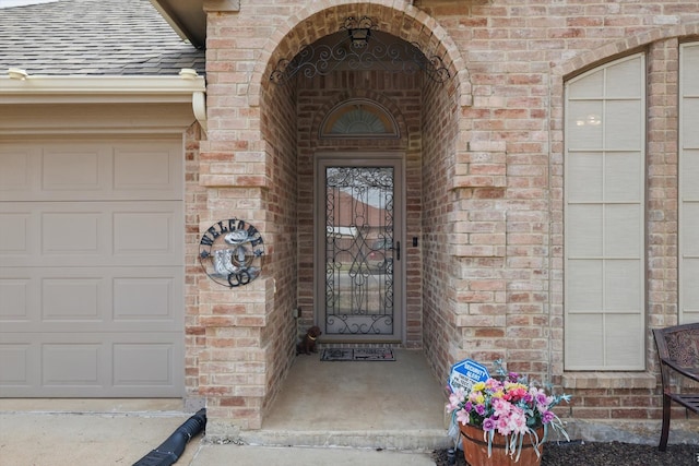 property entrance featuring a garage, brick siding, and roof with shingles