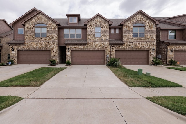 townhome / multi-family property featuring stone siding, driveway, a shingled roof, and a garage