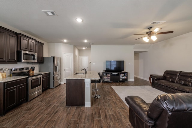 kitchen with visible vents, dark wood-type flooring, open floor plan, a kitchen breakfast bar, and stainless steel appliances