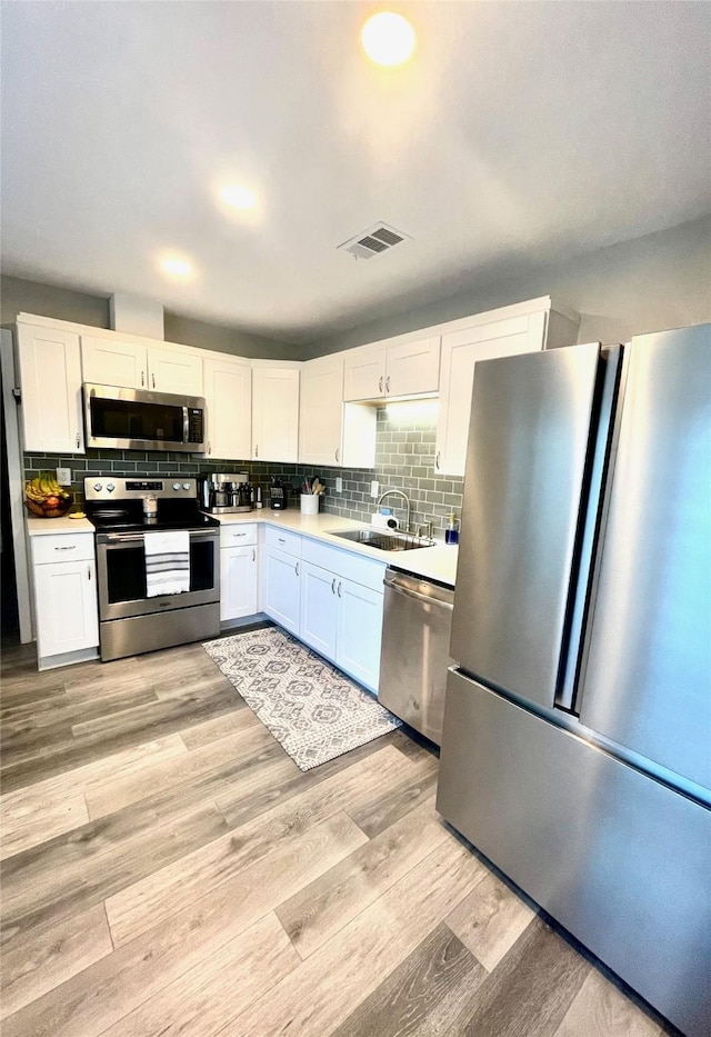 kitchen with a sink, decorative backsplash, stainless steel appliances, white cabinetry, and light wood-type flooring