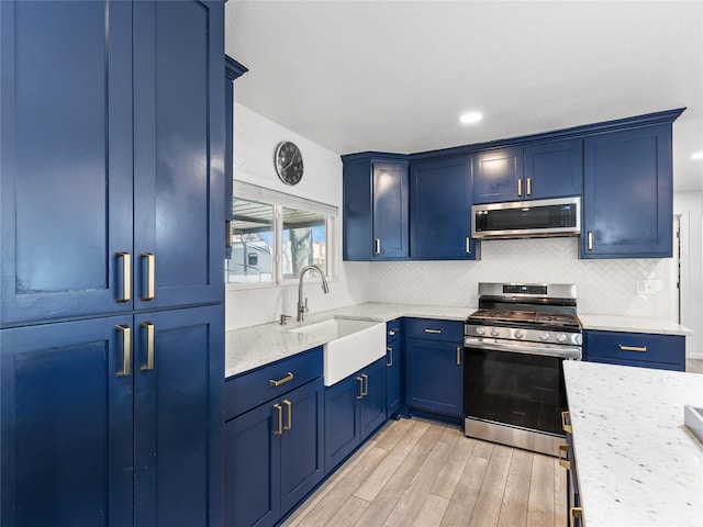 kitchen with a sink, blue cabinetry, tasteful backsplash, stainless steel appliances, and light wood-style floors