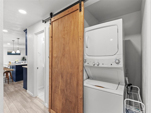 laundry area featuring light wood finished floors, laundry area, recessed lighting, stacked washer and dryer, and a barn door