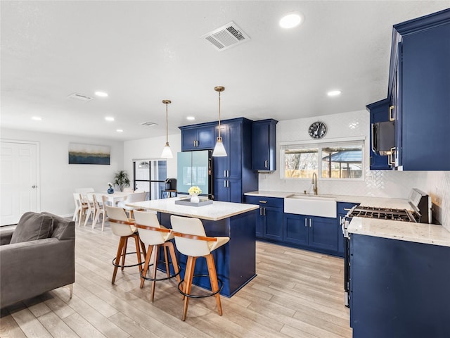 kitchen featuring visible vents, a breakfast bar, freestanding refrigerator, a sink, and blue cabinets