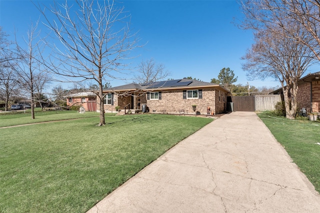 single story home with a gate, concrete driveway, a front yard, brick siding, and solar panels