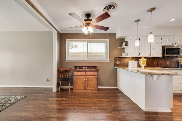 kitchen with light stone countertops, visible vents, dark wood finished floors, decorative backsplash, and stainless steel microwave