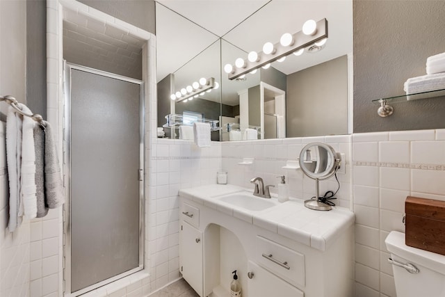 bathroom with vanity, a stall shower, tile walls, toilet, and a textured wall