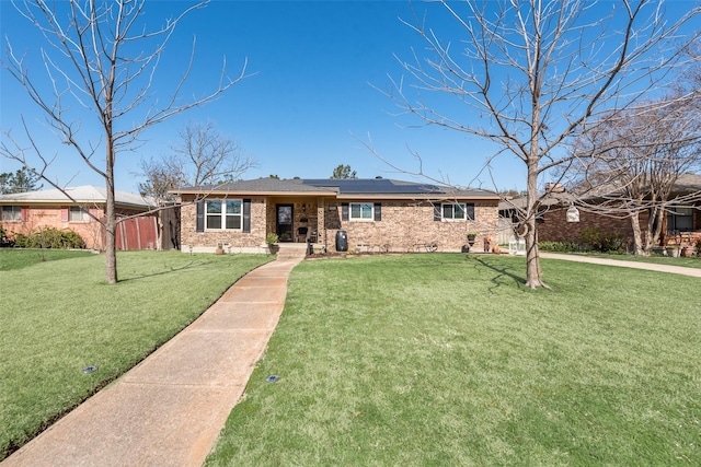 single story home with roof mounted solar panels, brick siding, and a front lawn