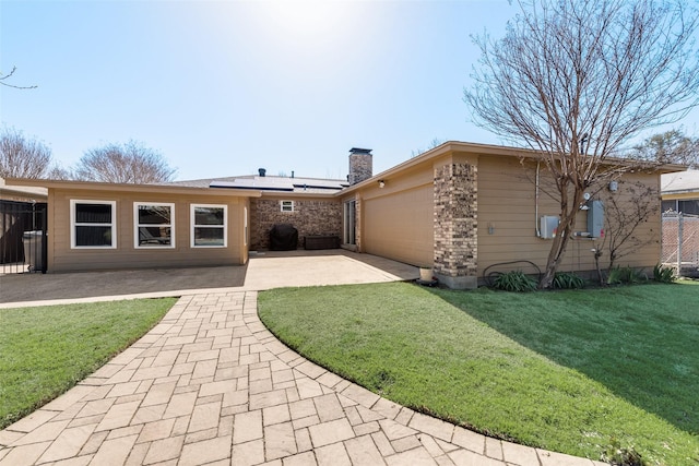 rear view of house with a patio, driveway, an attached garage, a chimney, and a lawn