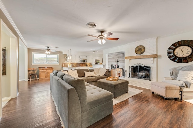 living room with visible vents, baseboards, hardwood / wood-style flooring, crown molding, and a brick fireplace