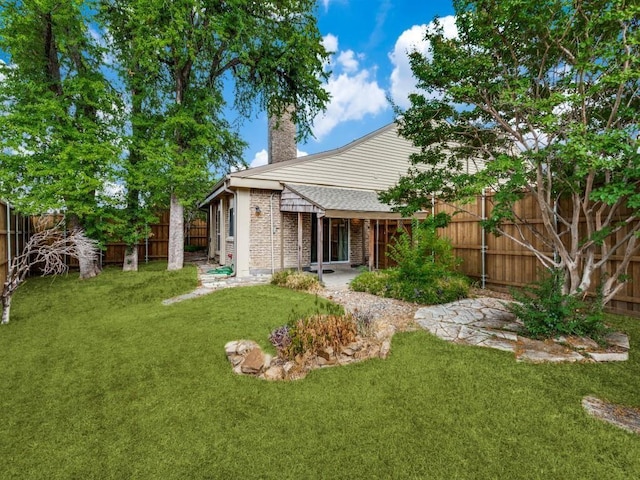 rear view of property featuring brick siding, a lawn, a fenced backyard, and a chimney