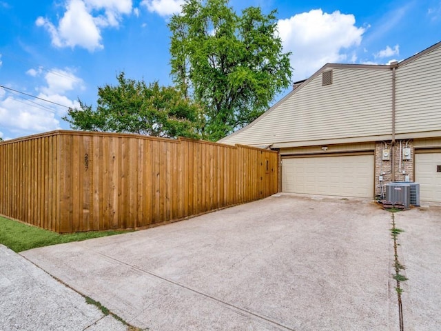 view of property exterior featuring central air condition unit, fence, a garage, and driveway