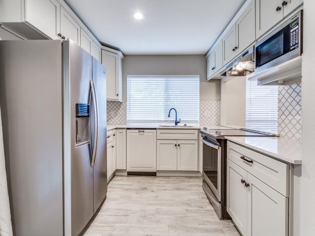 kitchen with a sink, stainless steel appliances, light countertops, light wood-style floors, and tasteful backsplash