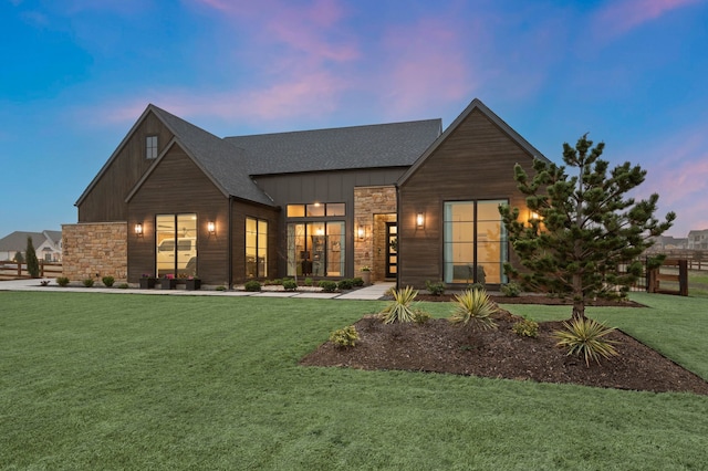 view of front of home with roof with shingles, board and batten siding, a front yard, and stone siding