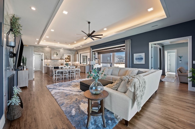 living room with a raised ceiling, ceiling fan, recessed lighting, and dark wood-style floors
