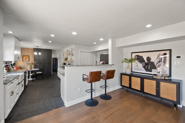 kitchen featuring white cabinets, light stone countertops, freestanding refrigerator, and a sink