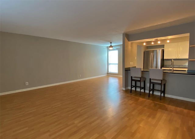 unfurnished living room with a sink, wood finished floors, baseboards, and ceiling fan