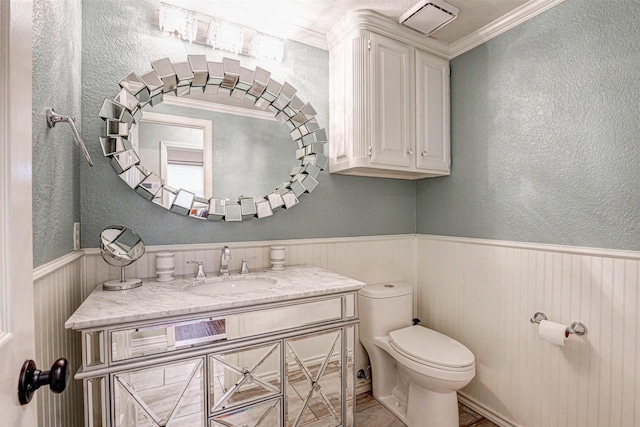 half bath with vanity, toilet, a textured wall, and wainscoting