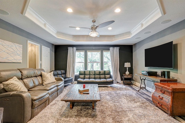 living area featuring a raised ceiling, wood finished floors, crown molding, baseboards, and ceiling fan