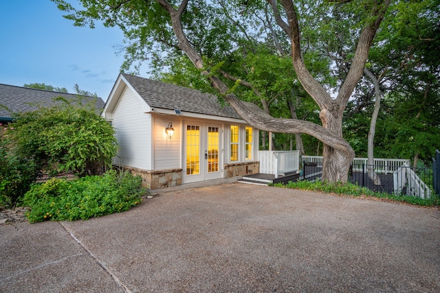 rear view of house with french doors, stone siding, fence, and a shingled roof