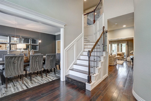 stairs with wood finished floors, a towering ceiling, and ornamental molding