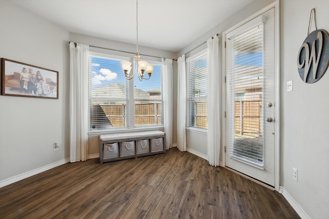 unfurnished dining area featuring baseboards, dark wood-type flooring, and an inviting chandelier