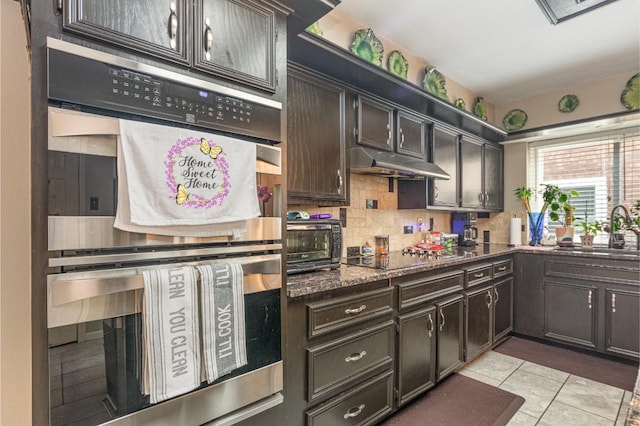 kitchen featuring under cabinet range hood, a sink, backsplash, double oven, and black electric stovetop