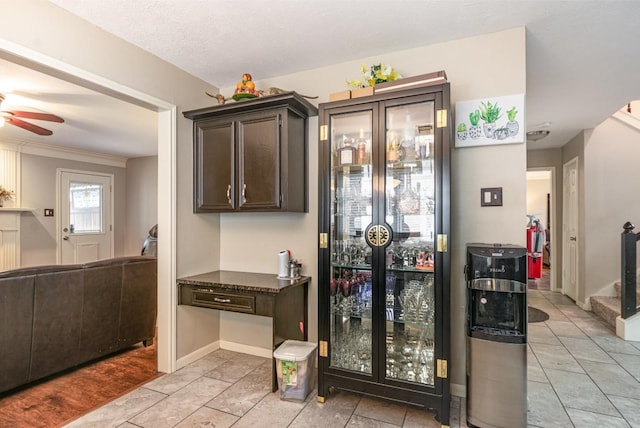 kitchen featuring a ceiling fan, dark stone counters, dark brown cabinetry, light tile patterned floors, and baseboards