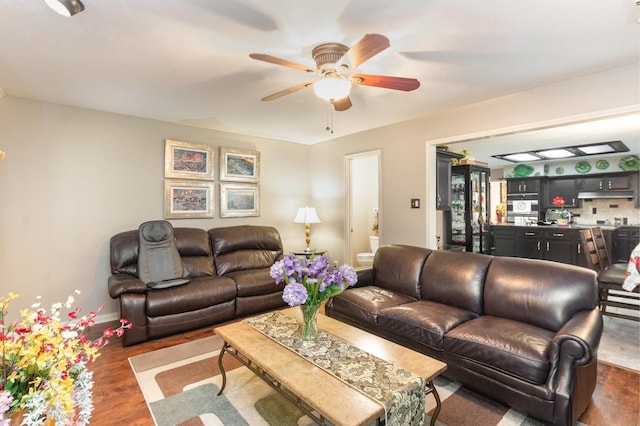 living area with baseboards, dark wood-type flooring, and a ceiling fan