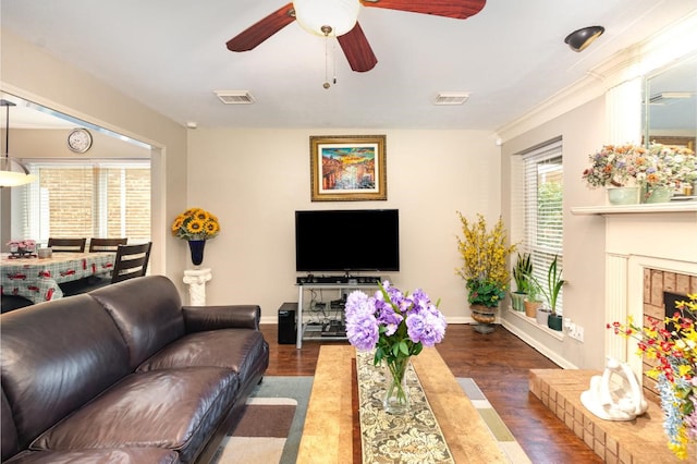 living room featuring visible vents, a fireplace with raised hearth, baseboards, and wood finished floors