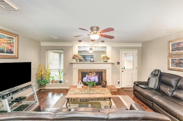 living room with visible vents, baseboards, a brick fireplace, and wood finished floors