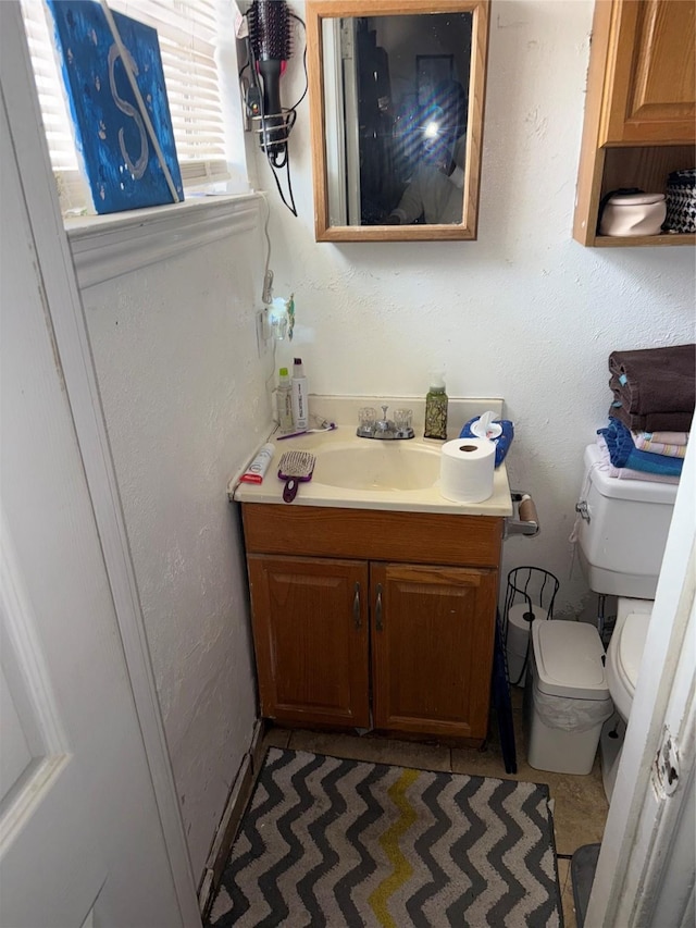 half bathroom featuring vanity, toilet, and a textured wall