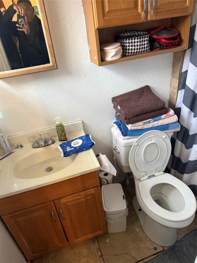 bathroom with toilet, vanity, and a textured wall