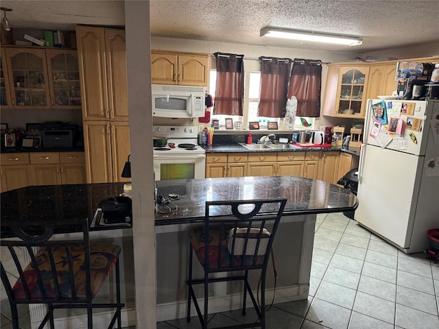 kitchen with a sink, dark countertops, white appliances, light tile patterned floors, and glass insert cabinets