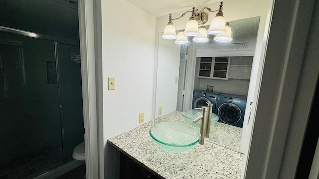 bathroom with toilet, an inviting chandelier, washing machine and dryer, and vanity