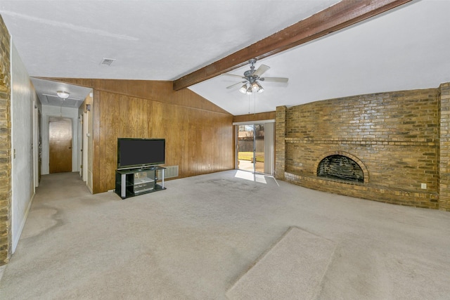 carpeted living room featuring vaulted ceiling with beams, wood walls, attic access, a fireplace, and a ceiling fan