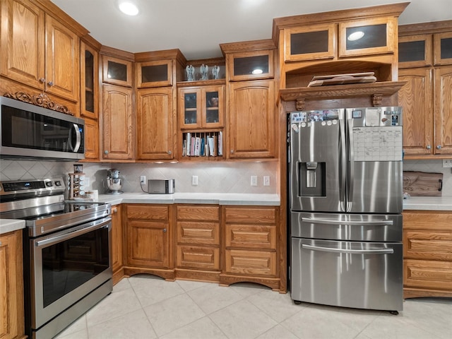 kitchen featuring stainless steel appliances, backsplash, brown cabinetry, and light countertops