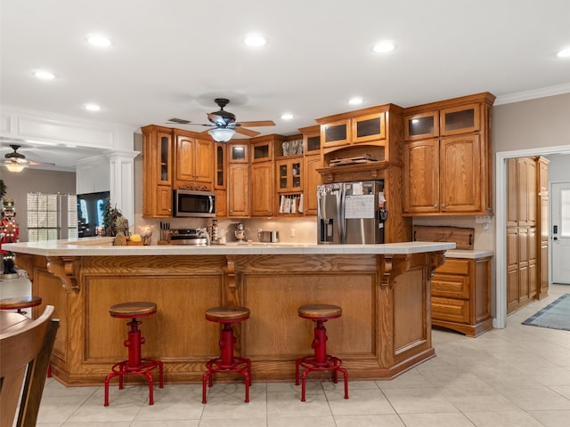 kitchen featuring a ceiling fan, appliances with stainless steel finishes, a breakfast bar, and brown cabinetry