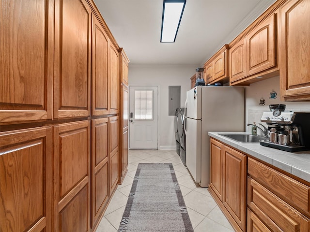 kitchen featuring washer and clothes dryer, a sink, freestanding refrigerator, tile countertops, and light tile patterned floors