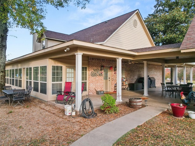 back of house with brick siding, a patio area, and roof with shingles