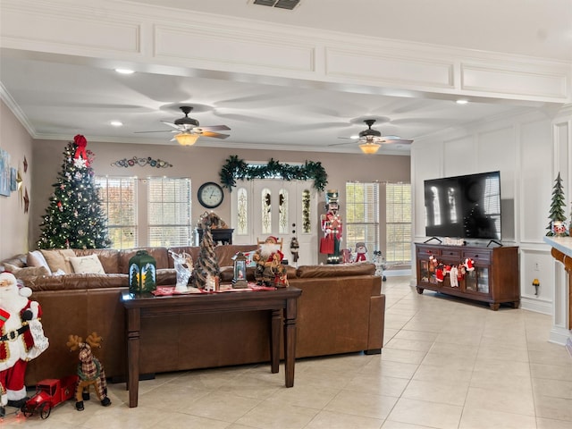 living area featuring light tile patterned floors, a ceiling fan, visible vents, ornamental molding, and a decorative wall